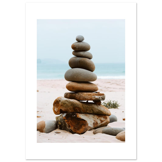 Balanced stack of smooth stones on a sandy beach with the ocean in the background – a calming, minimalist coastal scene perfect for interiors focused on wellness, meditation, or modern natural style